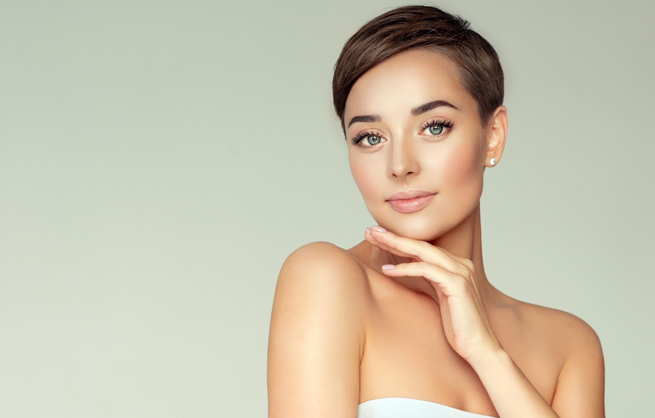Young, brown haired woman with short stylish haircut, clean fresh skin and light, delicate makeup is touching the face by slender fingers. Cosmetology. Laser Treatments 2 1 scaled Laser Treatments in Westborough, Salem, & Naples